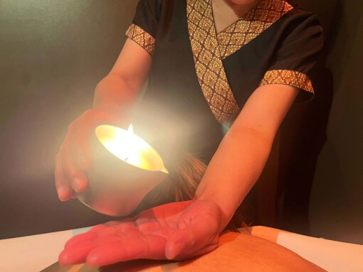 la masseuse verse dans sa main l'huile issue d'une bougie allumée. en dessous une femme est couchée sur le ventre.