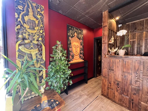 zone d'accueil du salon avec des plantes vertes. le mur en rouge sombre présente des décoration à l'effigie de Boudha.